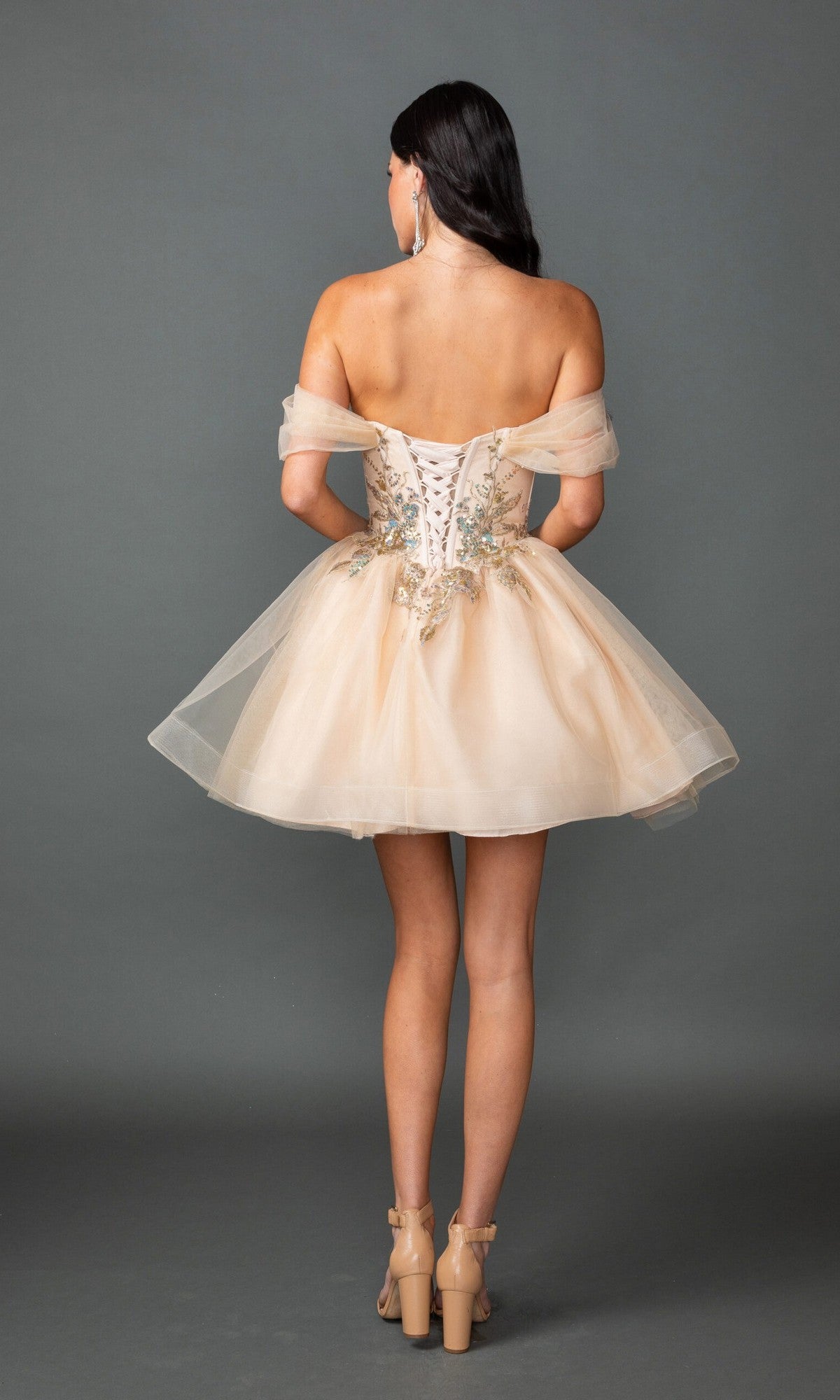 A woman faces away, wearing the Dancing Queen 3423 short prom dress—off-the-shoulder with an A-line skirt, beaded embroidery, lace-up back—and beige high-heeled sandals.
